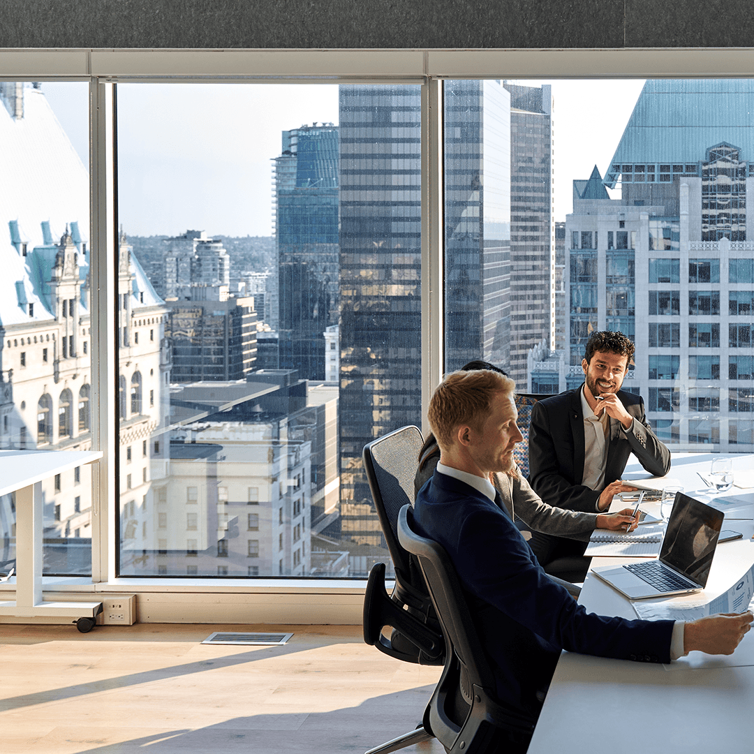 Two business professionals working on laptops in a modern office overlooking a city skyline. Two business professionals working on laptops in a modern office overlooking a city skyline.