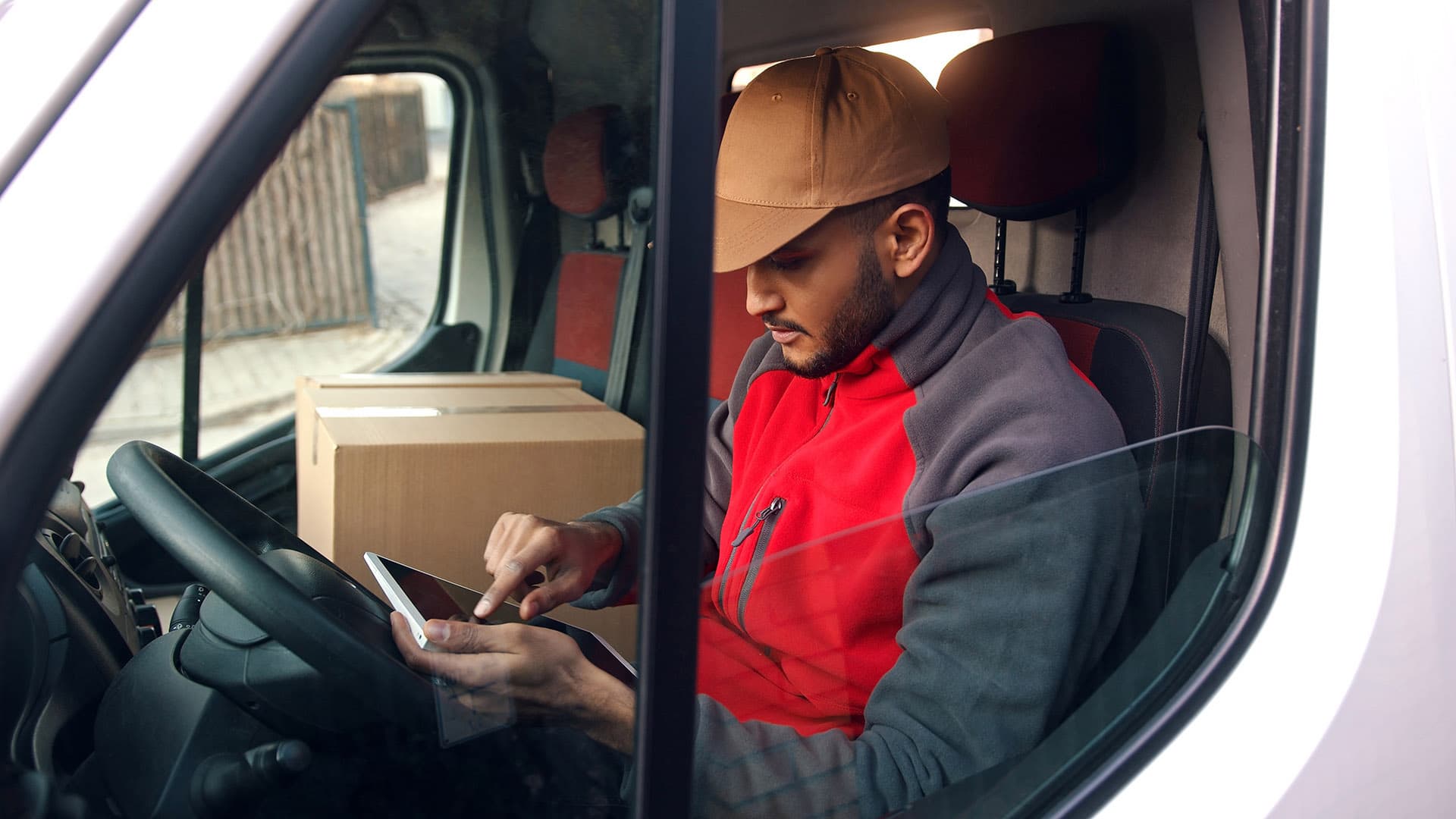 Un livreur utilisant une tablette alors qu’il est assis à l’intérieur d’une camionnette. Un livreur utilisant une tablette alors qu’il est assis à l’intérieur d’une camionnette.
