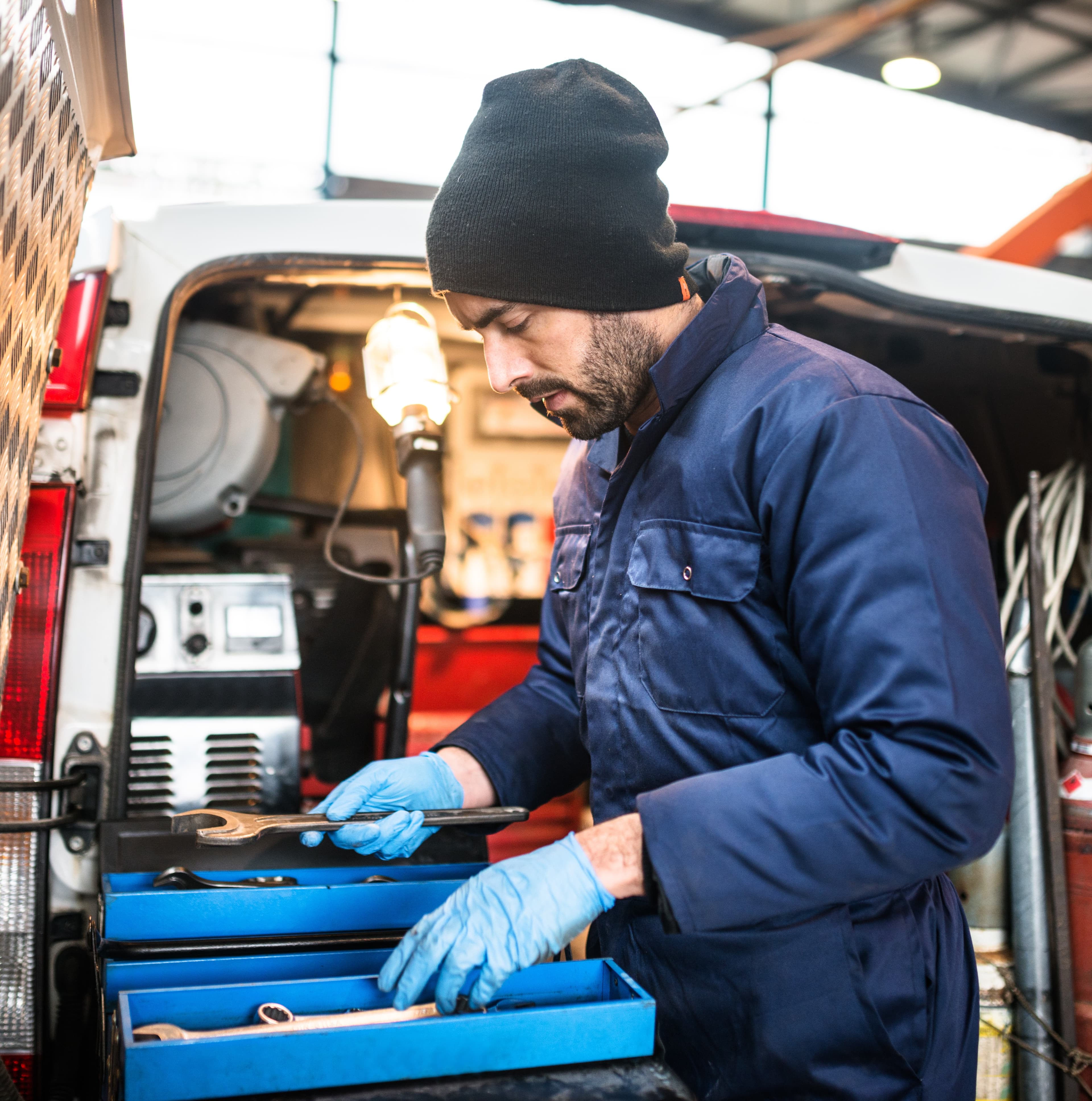 Fleet maintenance technician working from a mobile service van, checking tools during vehicle repair. Fleet maintenance technician working from a mobile service van, checking tools during vehicle repair.