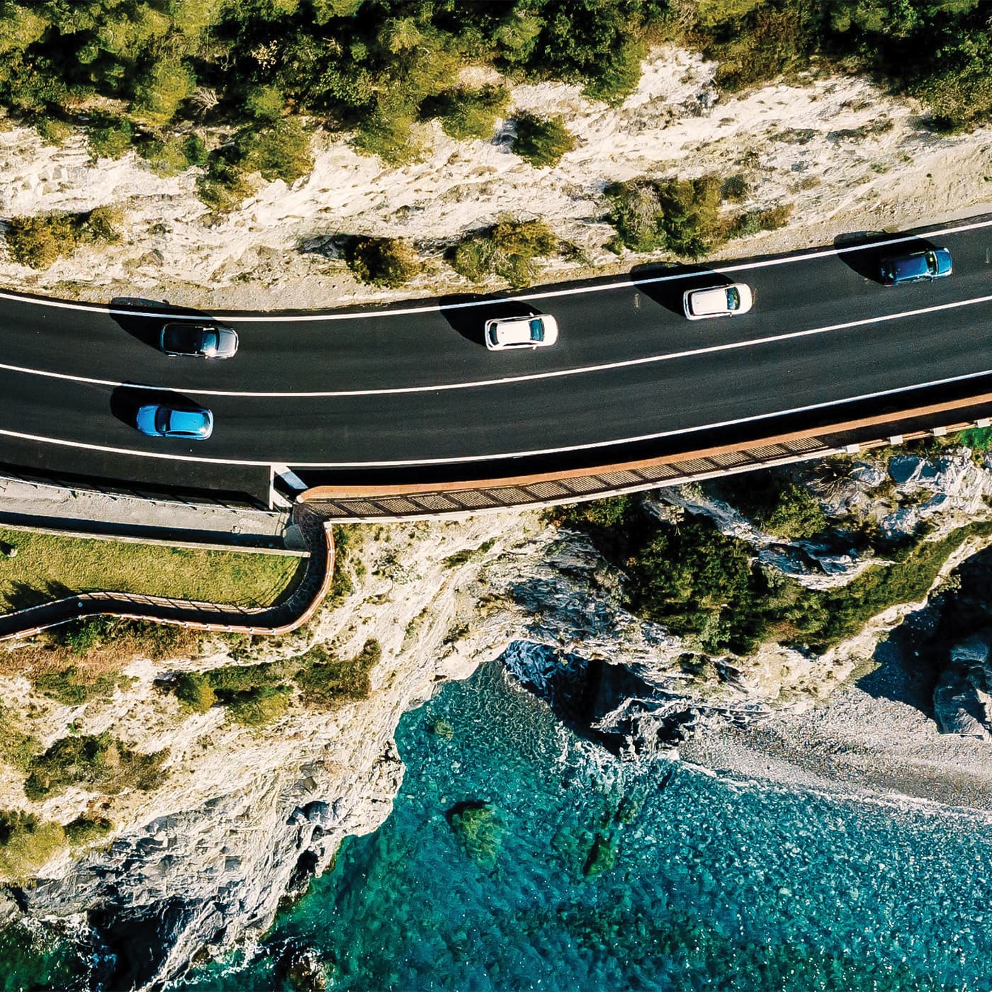 An aerial photo of an ocean-side road with cars travelling on both sides of the road. An aerial photo of an ocean-side road with cars travelling on both sides of the road.