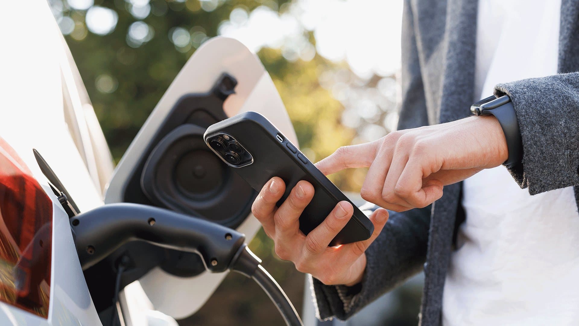Une personne utilise un téléphone intelligent pendant la recharge d’un véhicule électrique. Une personne utilise un téléphone intelligent pendant la recharge d’un véhicule électrique.