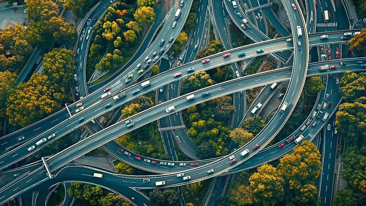 Aerial view of a complex multi-level highway interchange surrounded by dense urban greenery and moving traffic. Aerial view of a complex multi-level highway interchange surrounded by dense urban greenery and moving traffic.