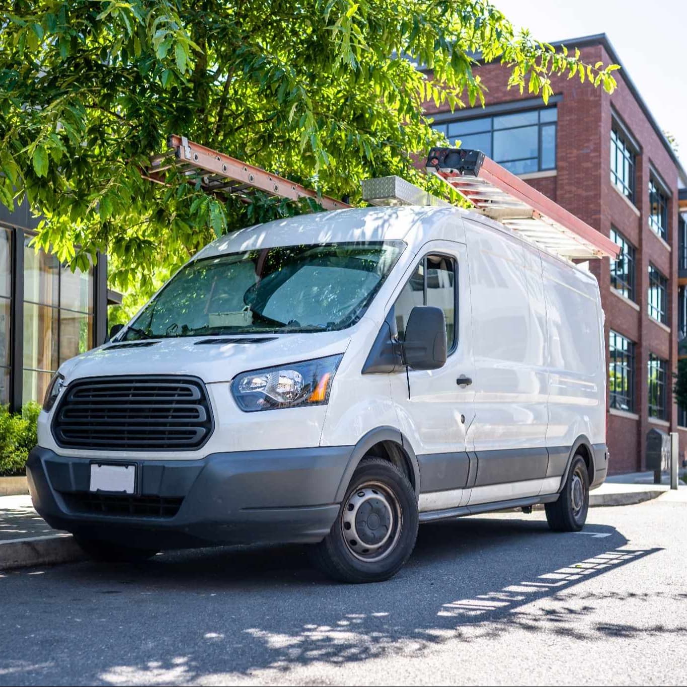 Fleet service van with a ladder on the roof on an urban city street with apartment buildings. Fleet service van with a ladder on the roof on an urban city street with apartment buildings.