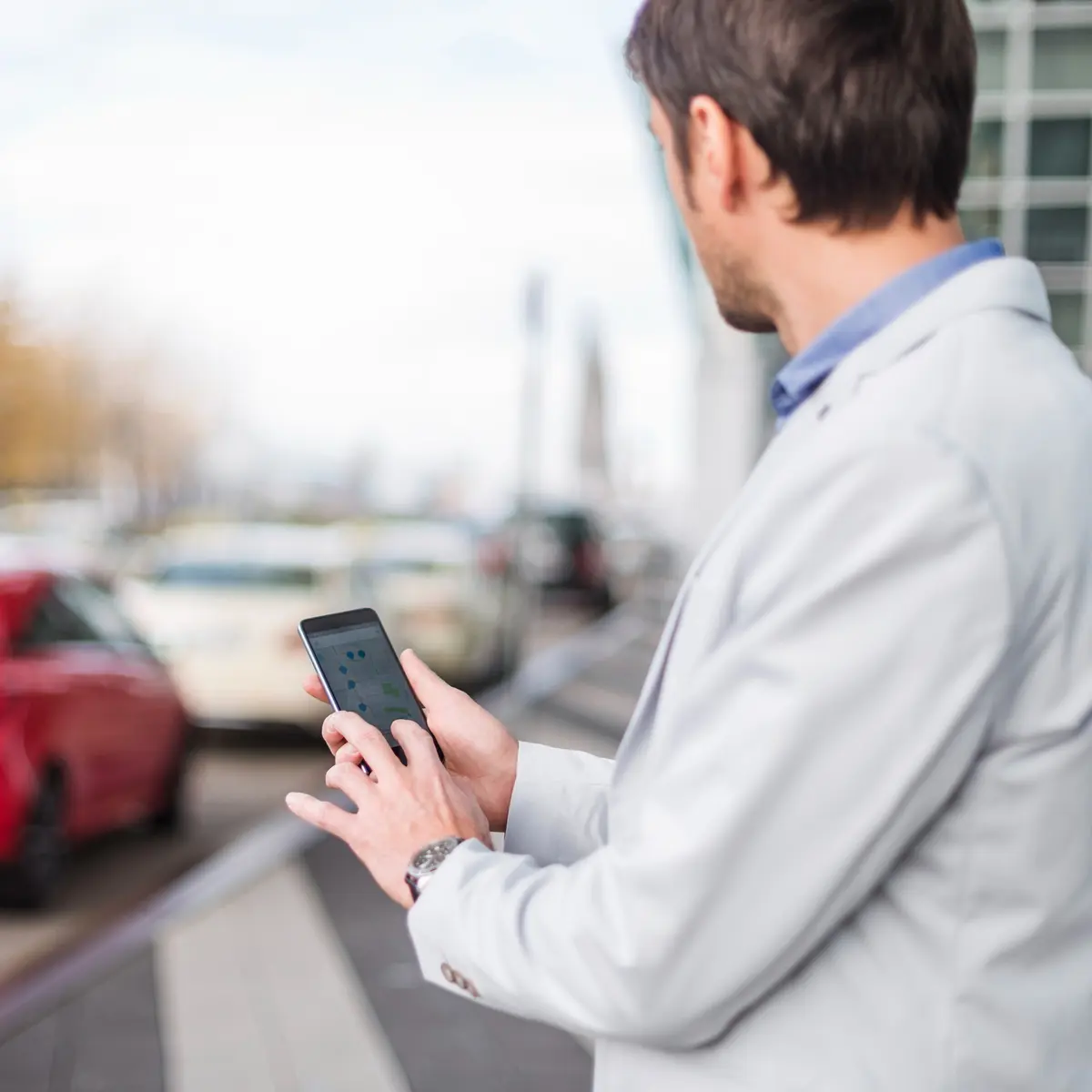 Man using a smartphone to view a vehicle location map while standing near parked cars. Man using a smartphone to view a vehicle location map while standing near parked cars.