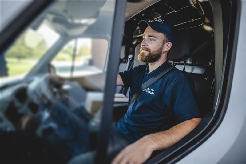 Delivery driver in branded uniform driving a cargo van, representing secure fleet operations and best practices to prevent cargo theft and ensure packages are delivered safely to customers. Delivery driver in branded uniform driving a cargo van, representing secure fleet operations and best practices to prevent cargo theft and ensure packages are delivered safely to customers.