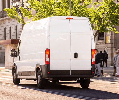 A white delivery van drives along a city street. A white delivery van drives along a city street.