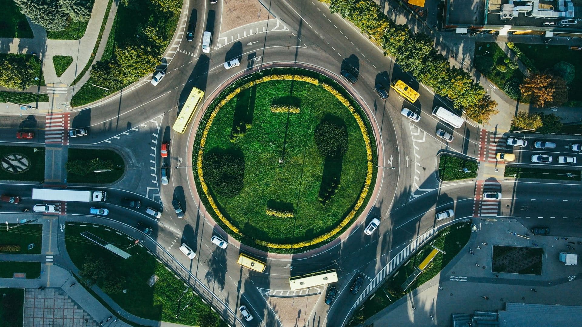 Aerial view of vehicles traveling around a landscaped urban roundabout. Aerial view of vehicles traveling around a landscaped urban roundabout.