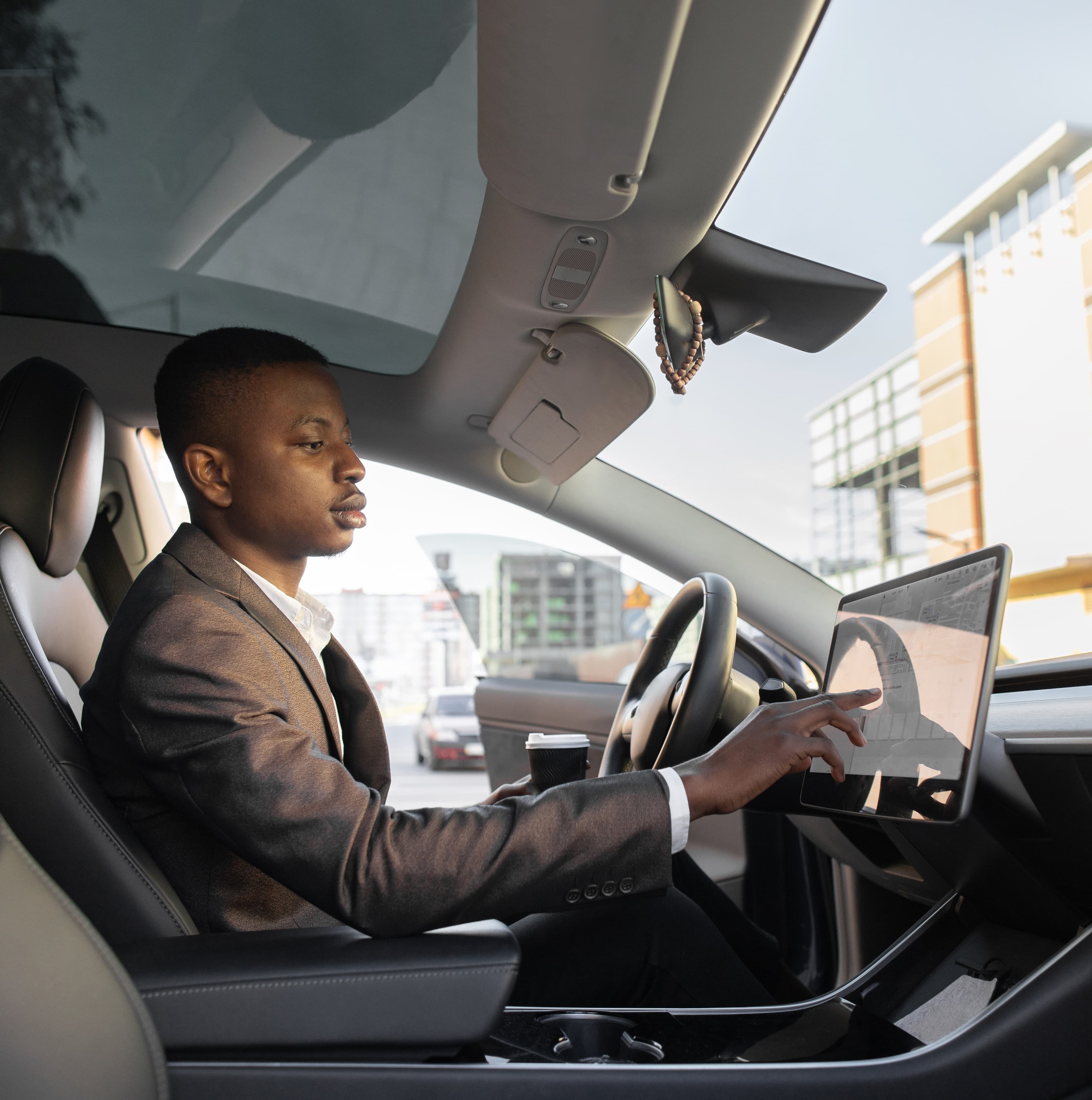 Driver in a modern car taps the central touchscreen navigation display while parked in an urban area, illustrating vehicle cybersecurity and connected in-vehicle systems. Driver in a modern car taps the central touchscreen navigation display while parked in an urban area, illustrating vehicle cybersecurity and connected in-vehicle systems.