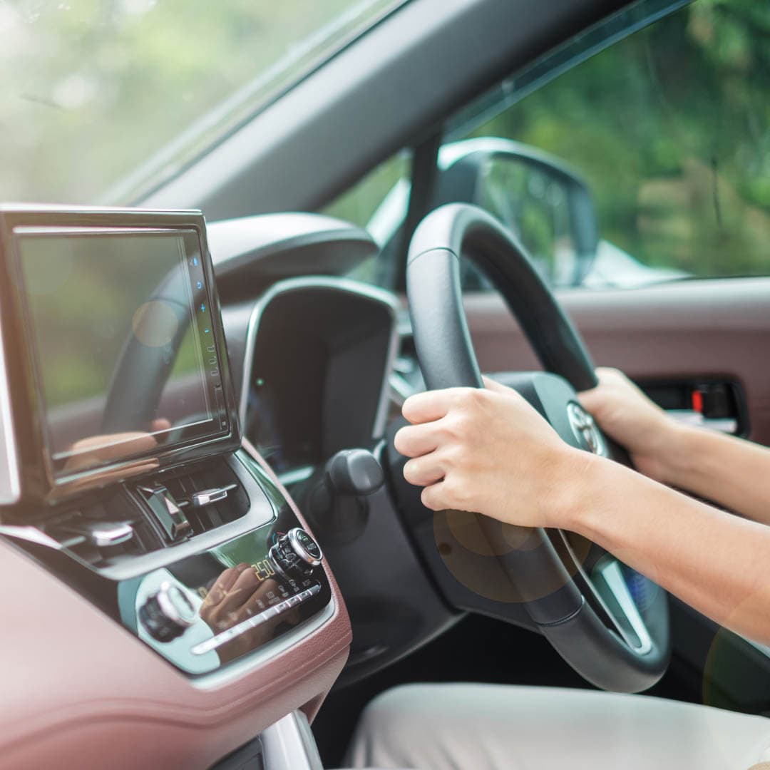 A woman driving a car on the road with her hands on the steering wheel. A woman driving a car on the road with her hands on the steering wheel.
