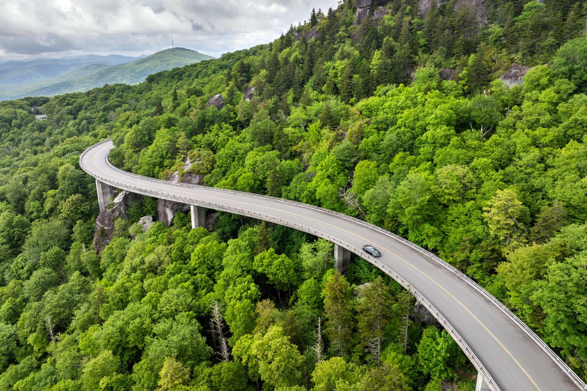Vue aérienne d'un véhicule circulant sur une route au cœur d'une forêt et d'un paysage montagneux. Vue aérienne d'un véhicule circulant sur une route au cœur d'une forêt et d'un paysage montagneux.